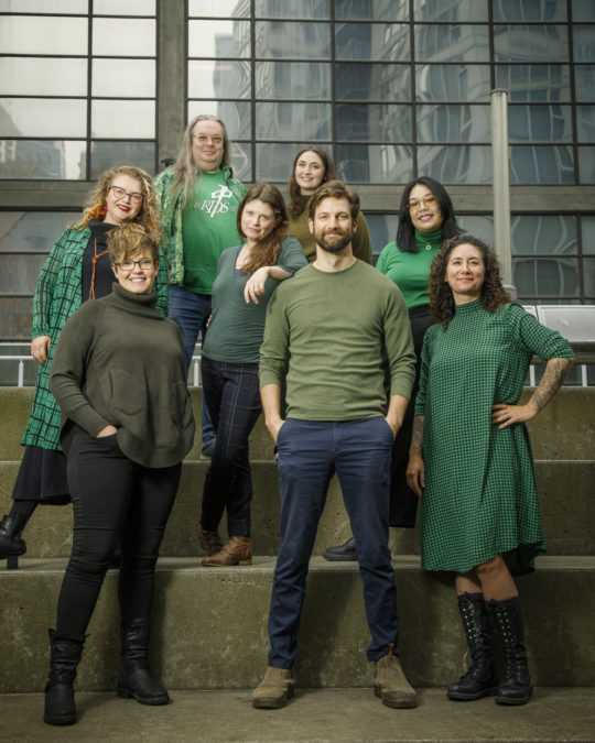 PuSh Festival team members, all dressed in green, stand together in front of the PuSh office