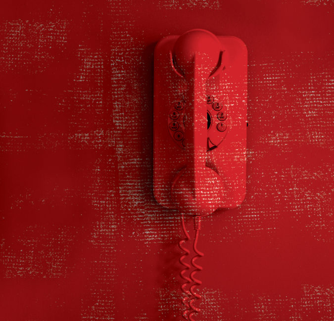 A red mid-century phone mounted on a red wall.