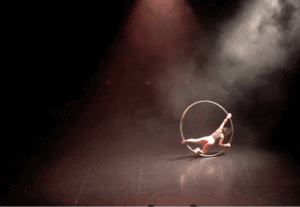 A woman balances inside a hula hoop as it rolls on the floor in a semi-circle