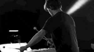 A black and white scene where a standing person in profile view plays the xylophone
