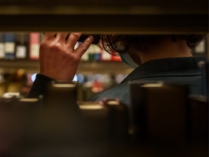 Partial view of two people, shot through the shelves of a library. One person holds a device up to the ear of another.