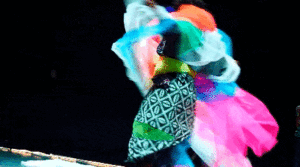 A person dressed in many overlapping colourful textiles dances in circles