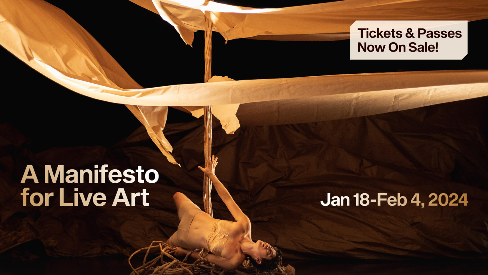 “A manifesto for live art. Tickets and Passes now on sale! Jan 18-Feb 4”. A performer lies on a pile of twisted branches holding up a wooden pole struck through floating layers of paper.