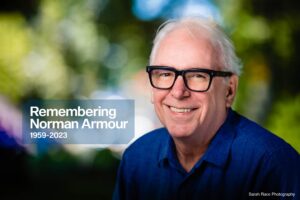 Headshot of Norman Armour smiling, wearing black glasses and blue button-down shirt, captioned "Remembering Norman Armour, 1959-2023"