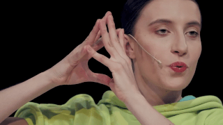 Closeup of a female performer speaking into a small headset, with fingers raised together beside her face.