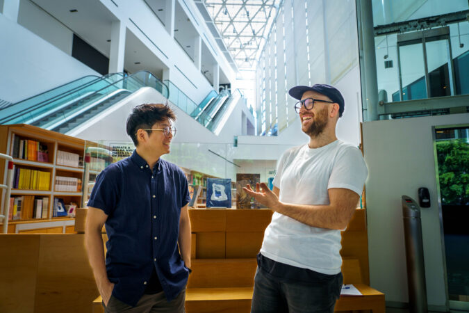Milton Lim and Patrick Blenkarn in the foreground, in the background are books on shelves and an escalator