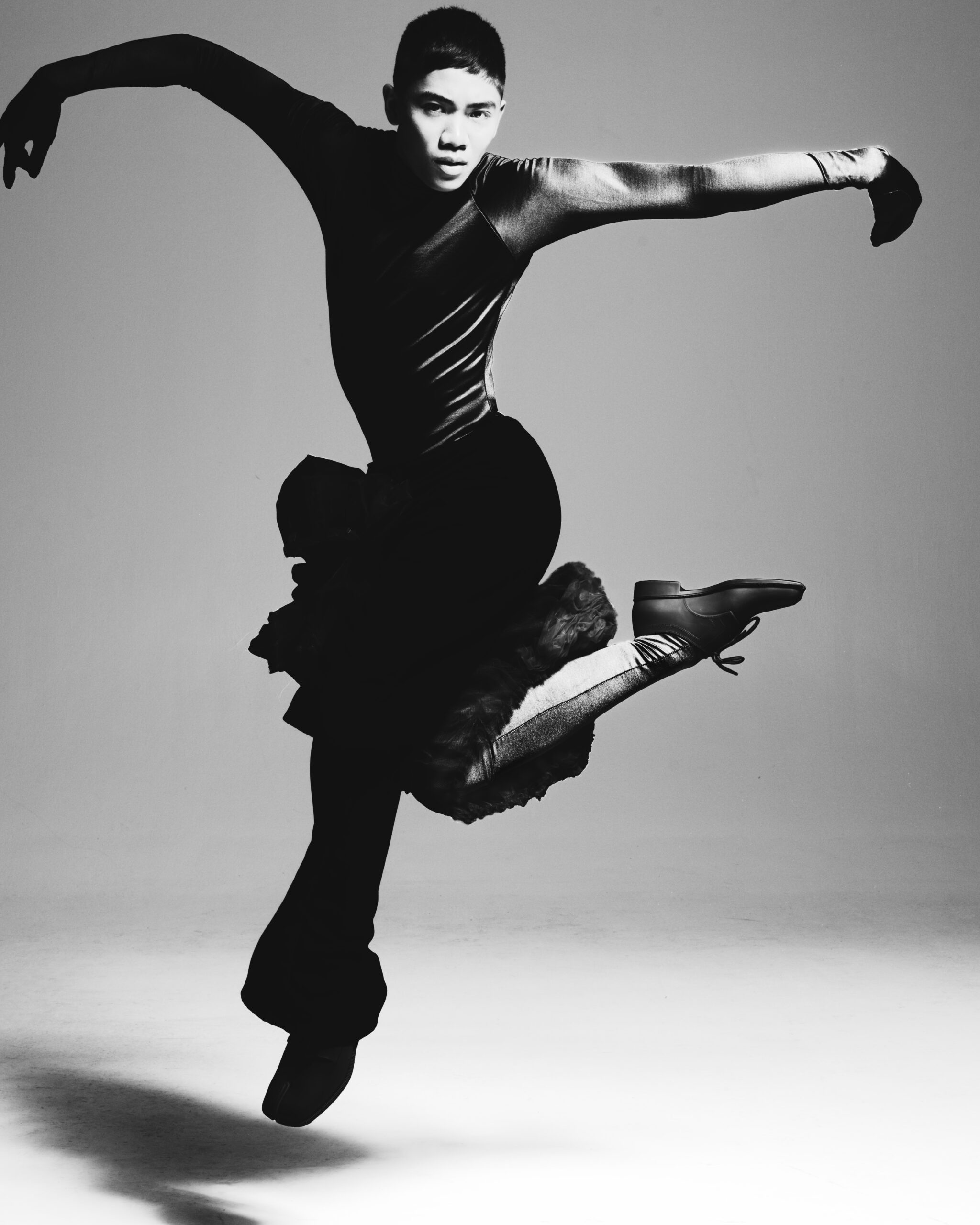 Posh in an artistic black and white photo, mid-dance with arms outstretched facing the camera.