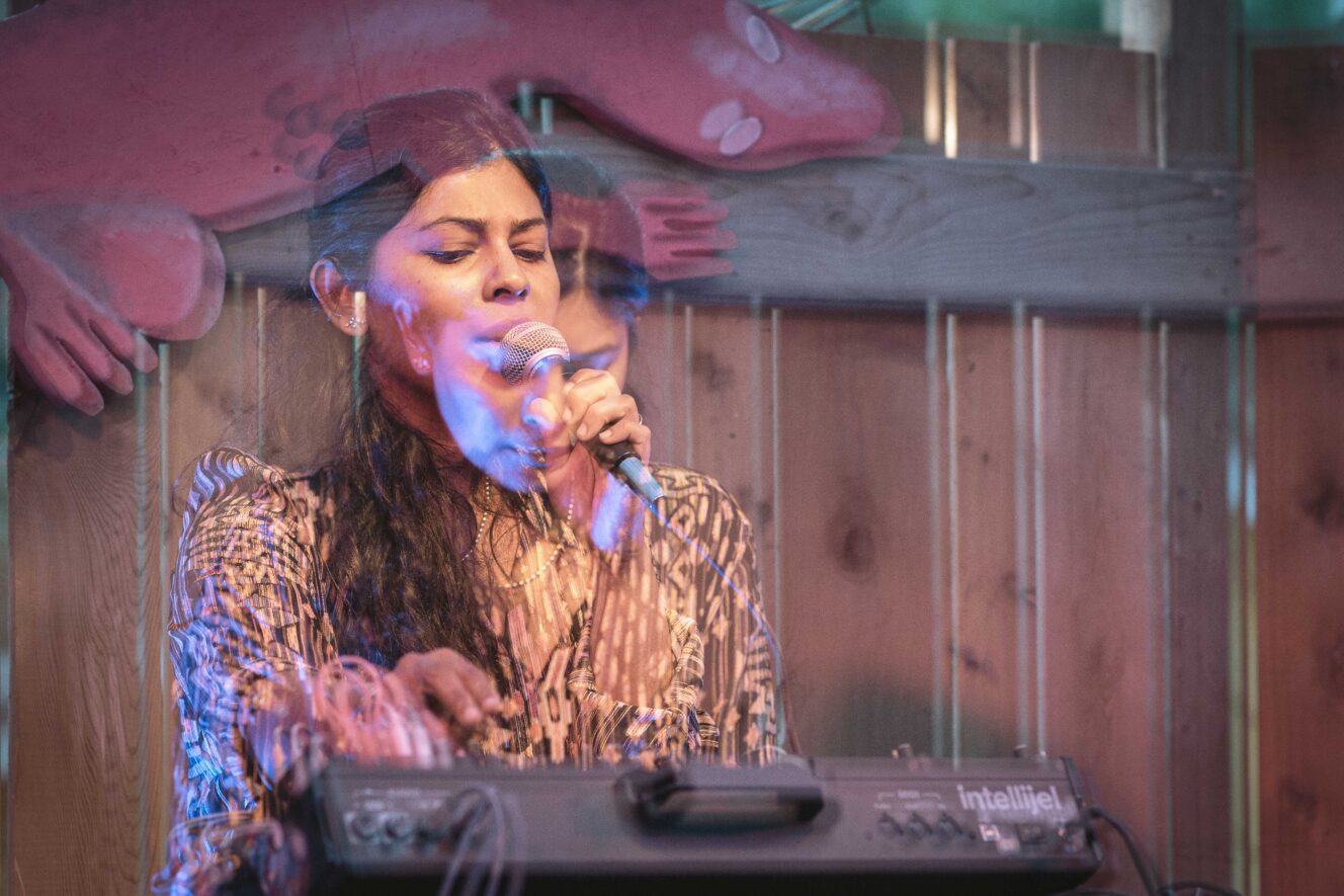 Double exposure image of Piu singing into a microphone over a console