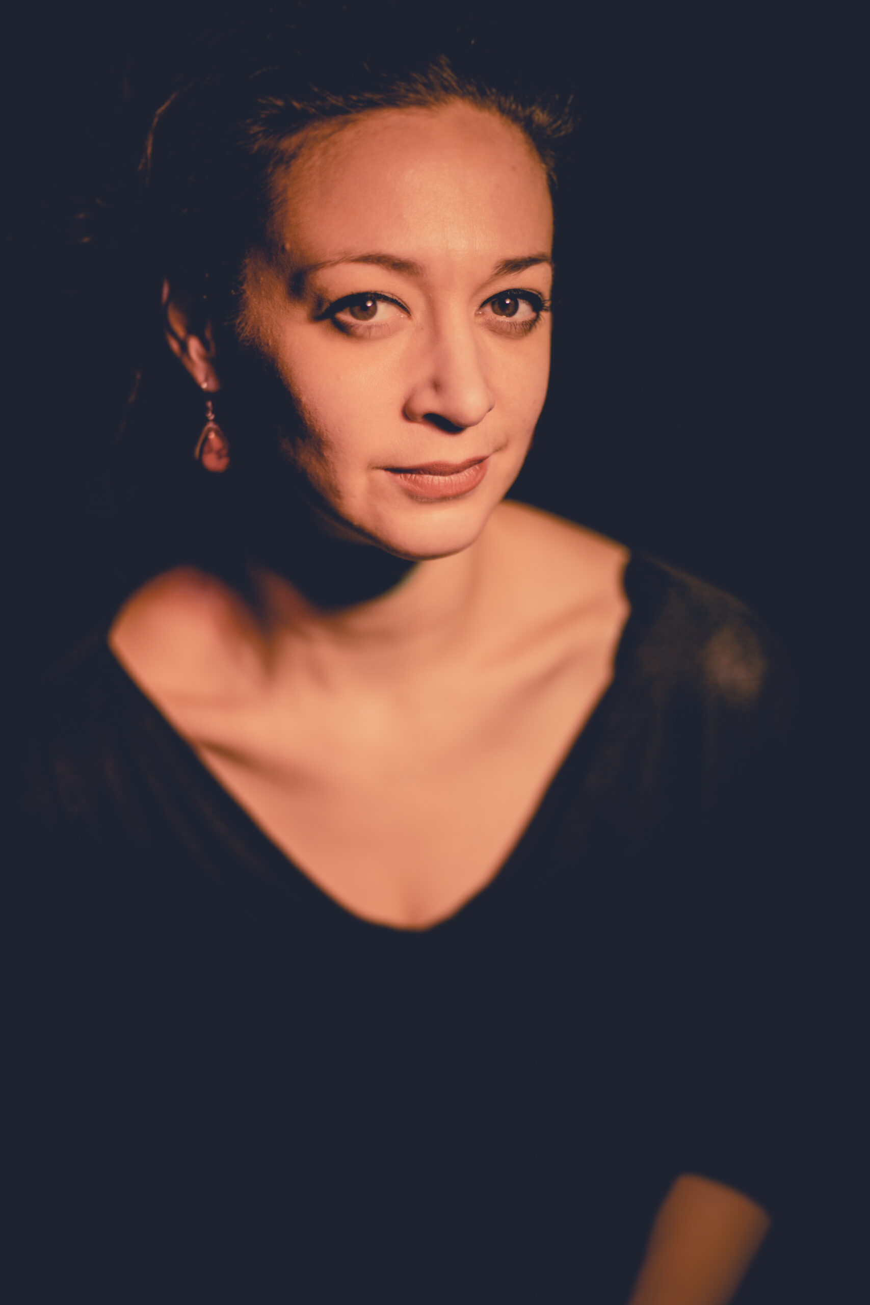 Andréane Leclerc, a woman wearing a black shirt and dangly earrings with hair pulled back. She is staring into the camera and poses against a dark background.