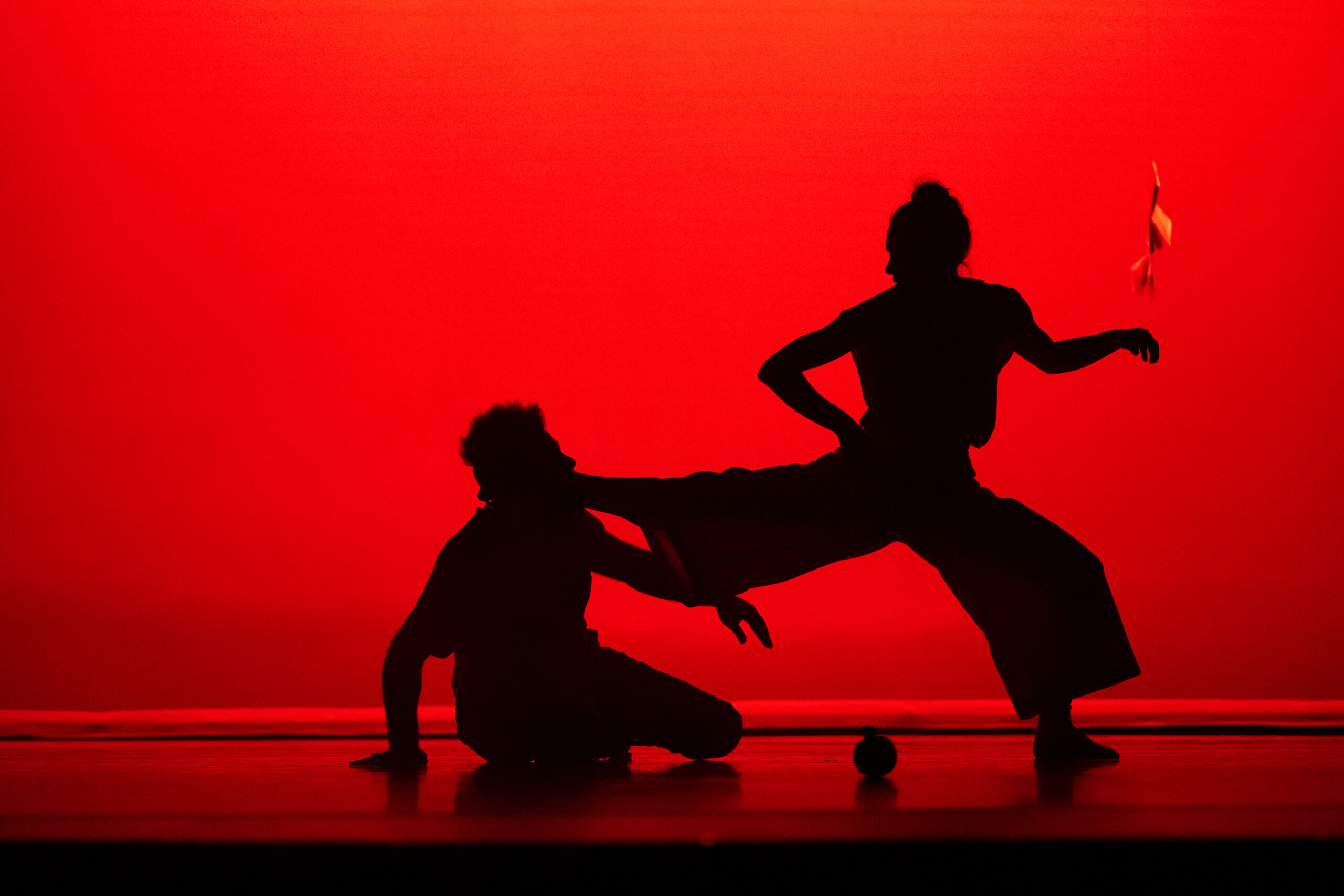 Two silhouetted dancers against a red stage.