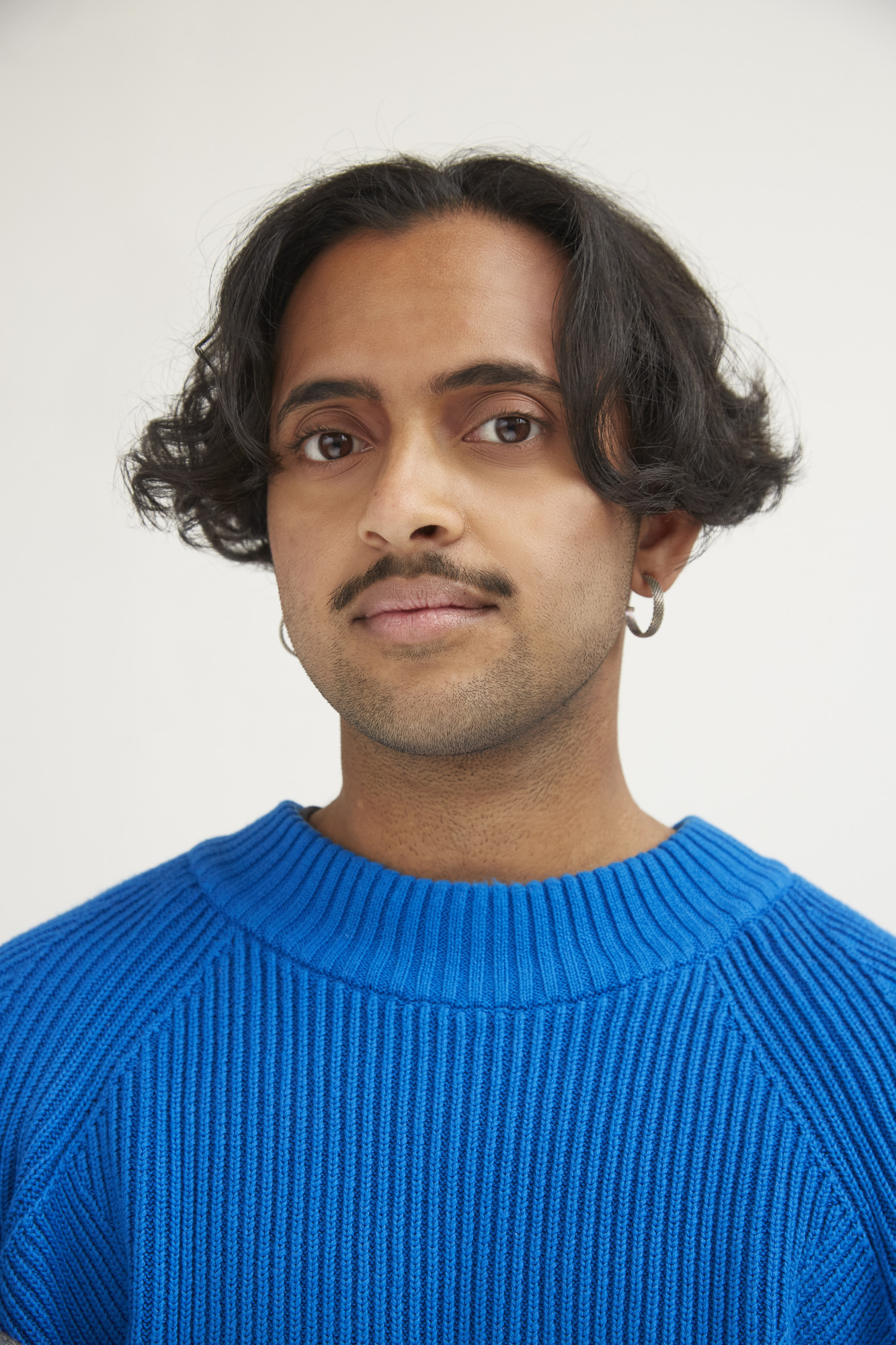 Headshot of Krishna Istha looking at the camera. Istha has a moustache, medium length wavy hair and is wearing a blue sweater.