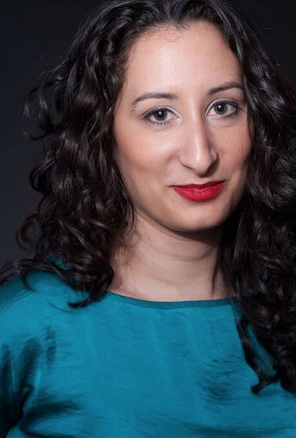 Closeup portraiat of a woman with long, dark curly hair. She has a slight smile and is wearing red lipstick and a silk teal shirt.